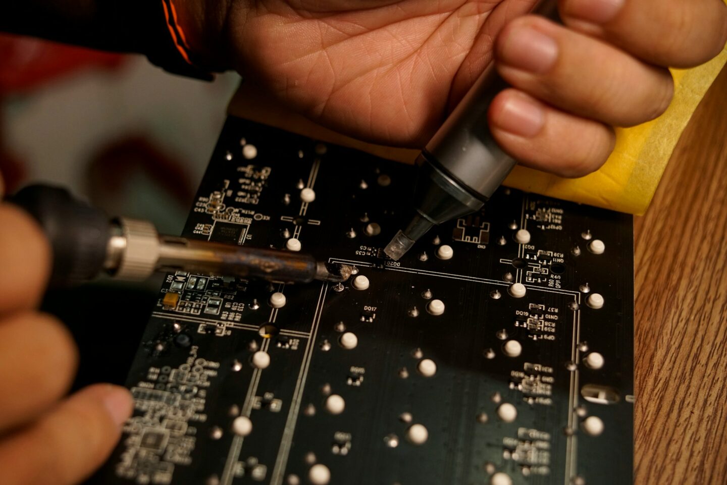 Hands using soldering tools on a circuit board during hardware hacking, electronics analysis, and reverse engineering work.