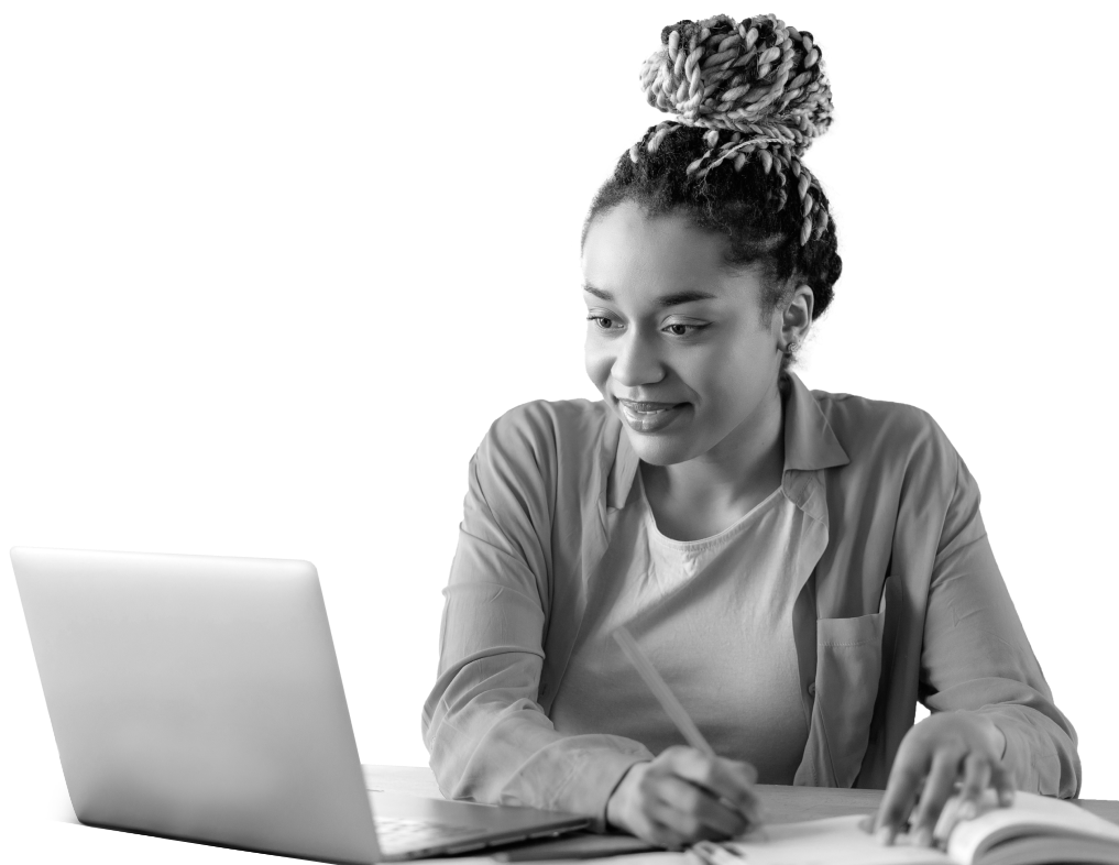 A woman sits at a desk, smiling and taking notes with a laptop open in front of her, conveying engagement in her cybersecurity training, in black and white.